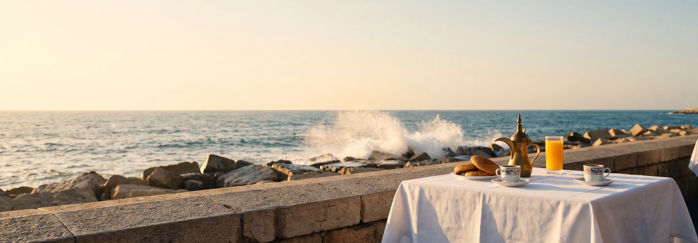 Waves breaking on the rocks below the sea wall at sunset, a table set by the water